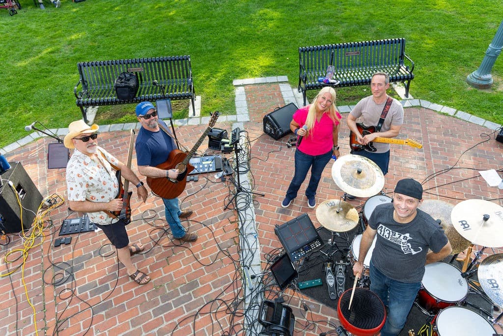 Aerial view of the full band setting up on a brick plaza between two park benches