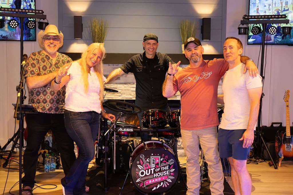 The five band members posing together indoors around the drum kit after a show