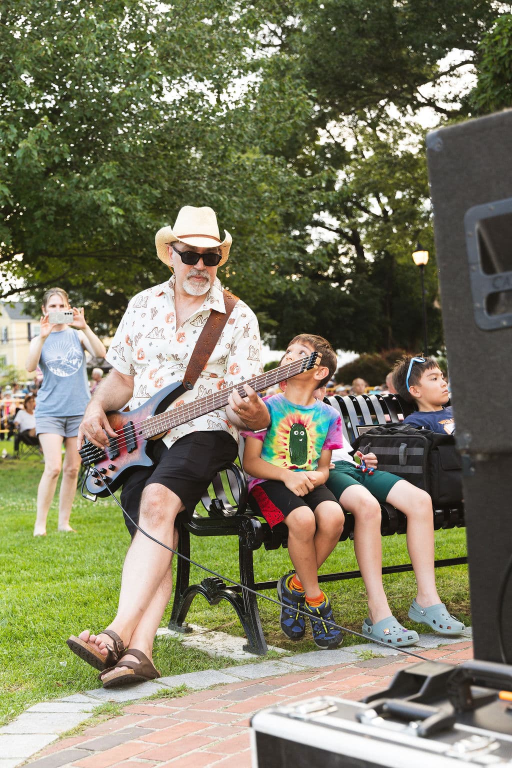 Bass player sitting on a park bench playing next to two kids watching closely