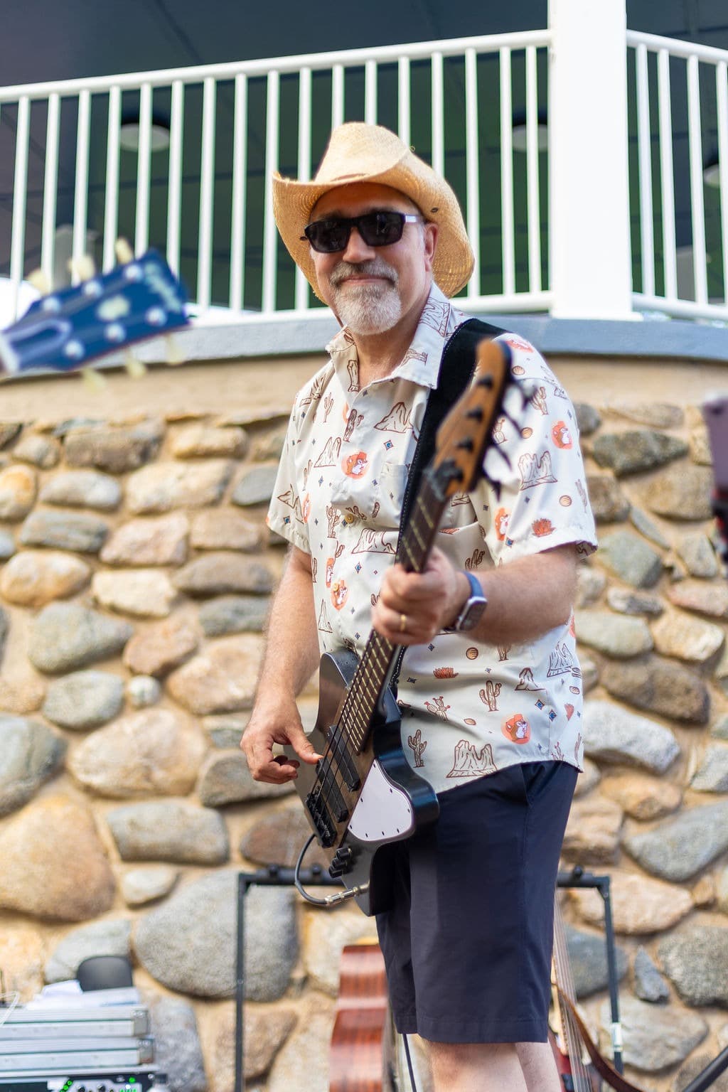 Bass player giving a peace sign in his cactus-print shirt and cowboy hat