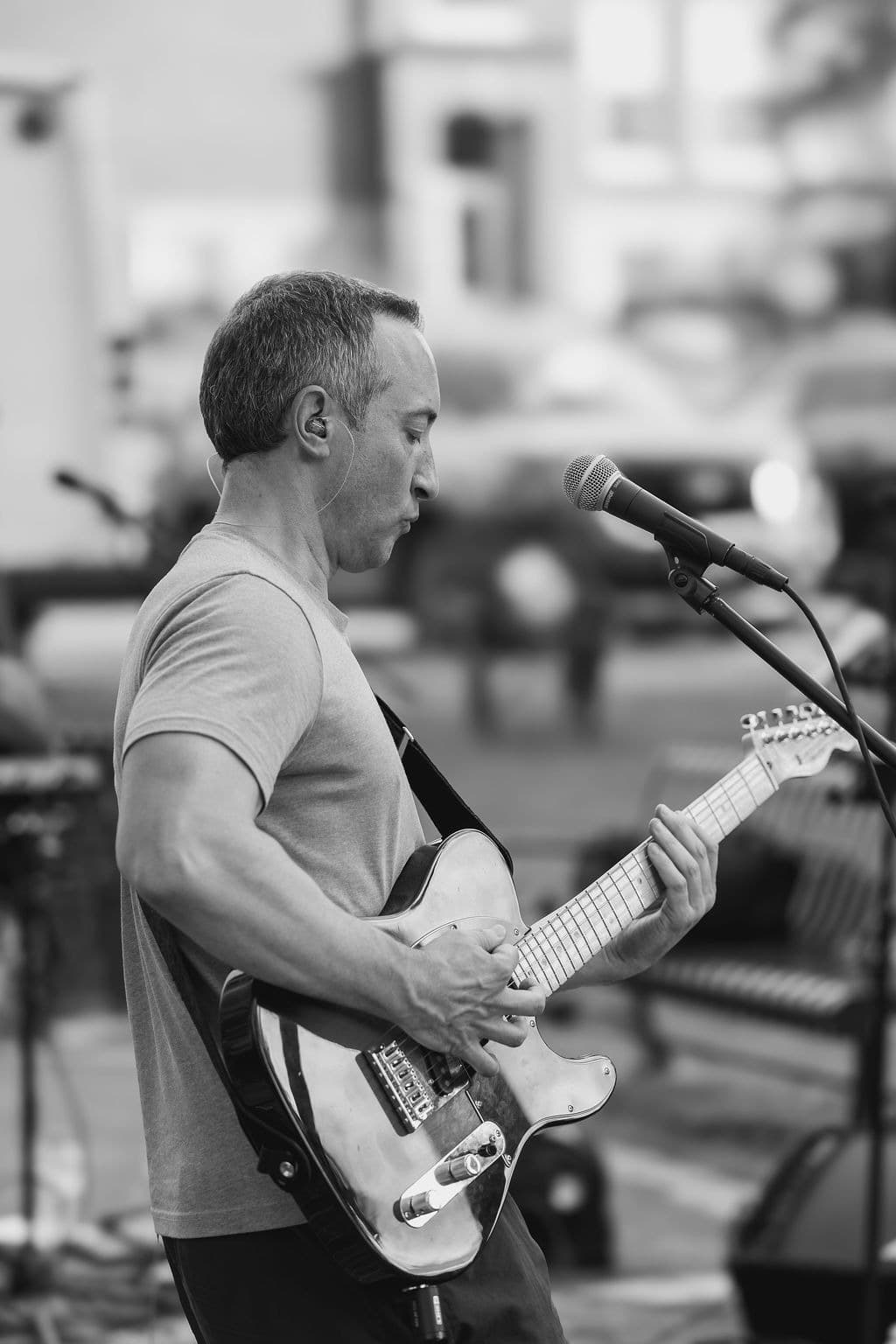Black-and-white portrait of the guitarist singing into the mic mid-song