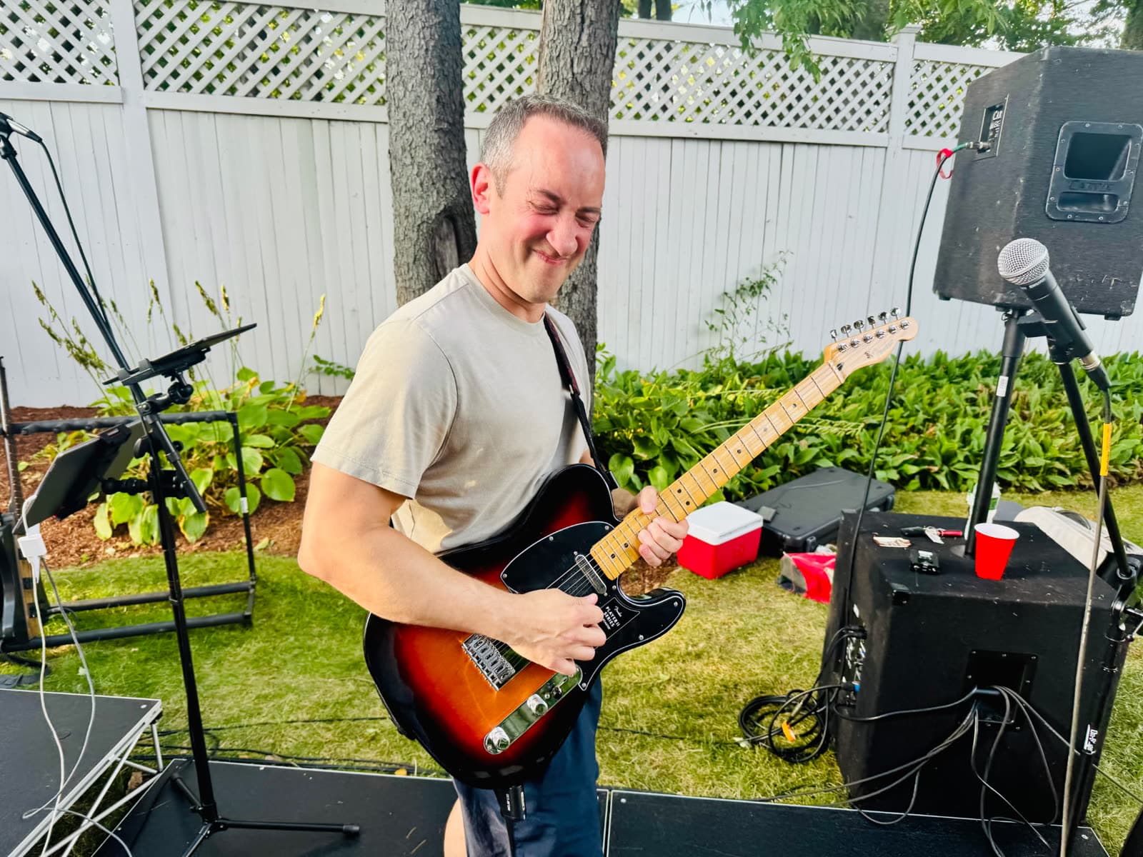 Guitarist playing with eyes closed at an outdoor backyard show