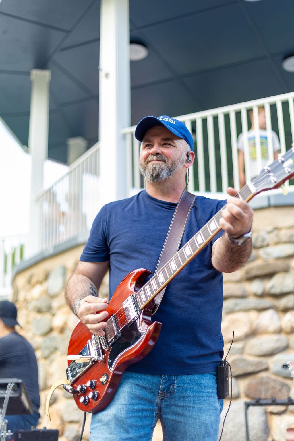 Guitarist playing under the gazebo roof with a kid watching from the balcony behind him