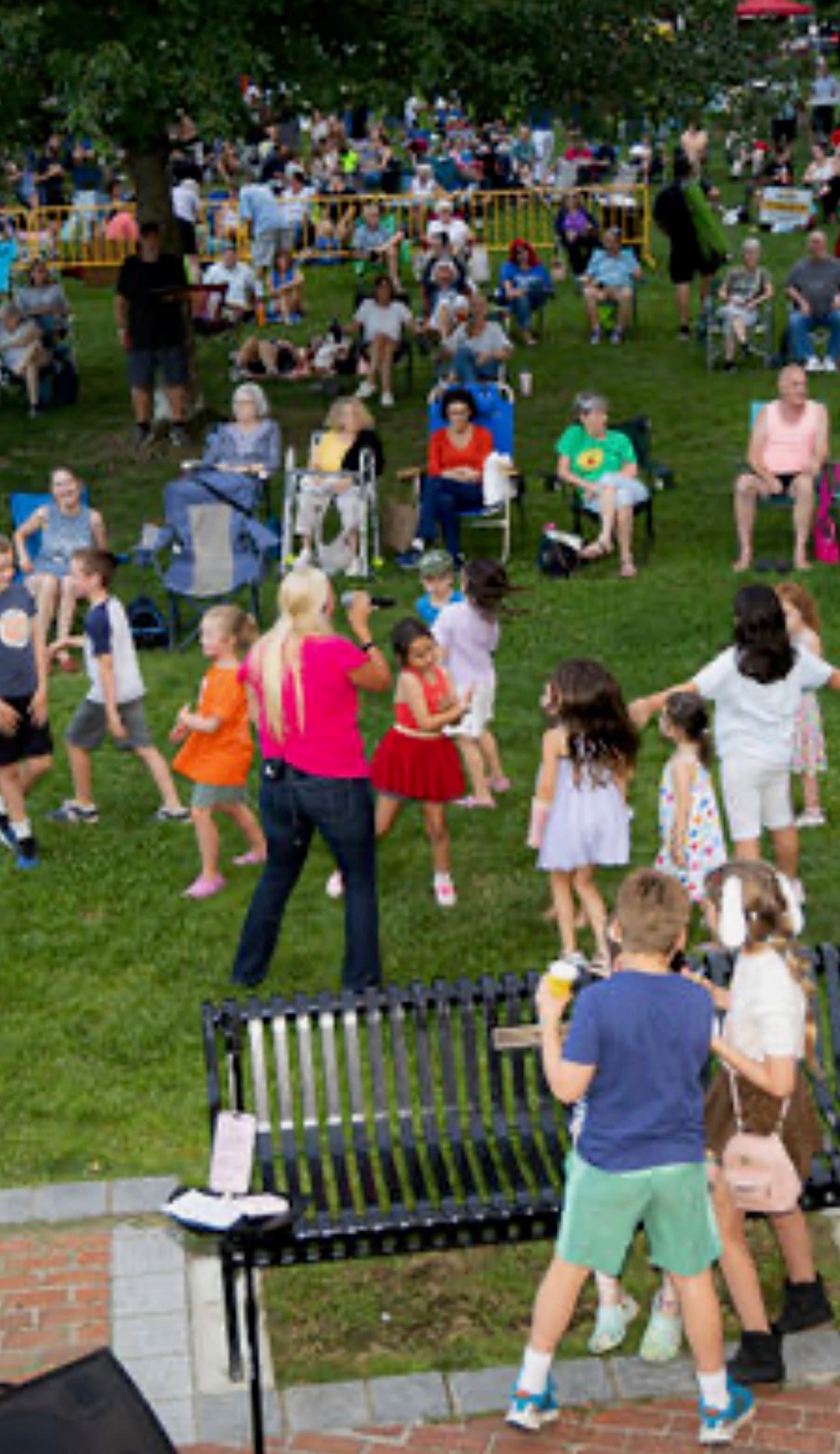 Kids dancing on the lawn as the singer leads the crowd, with a packed town common behind them