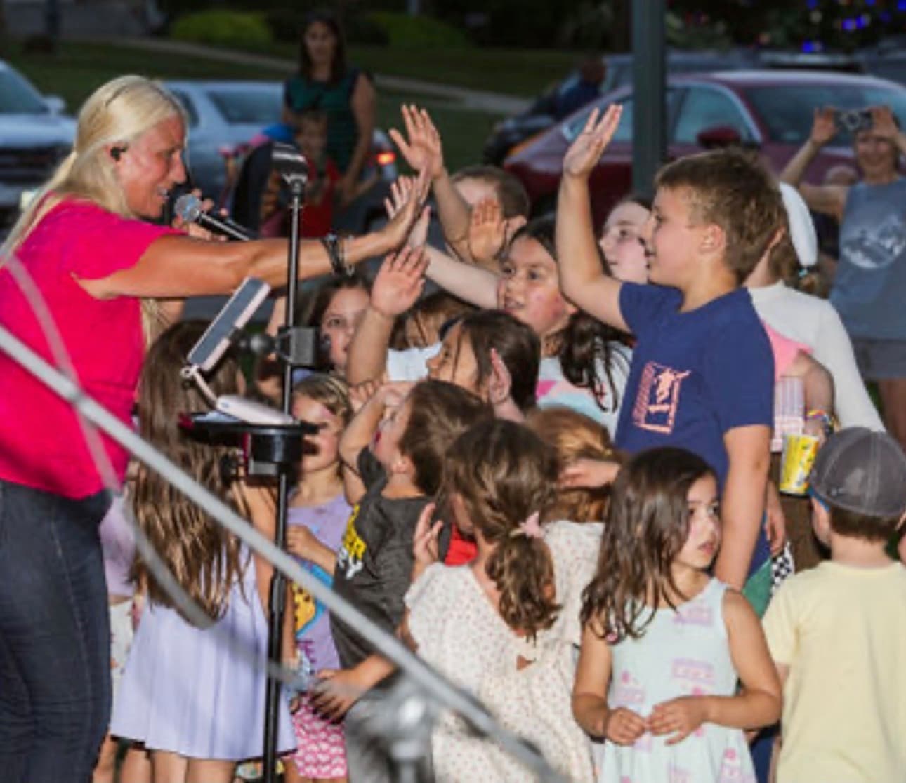 Singer cheering with a close group of kids reaching up toward her