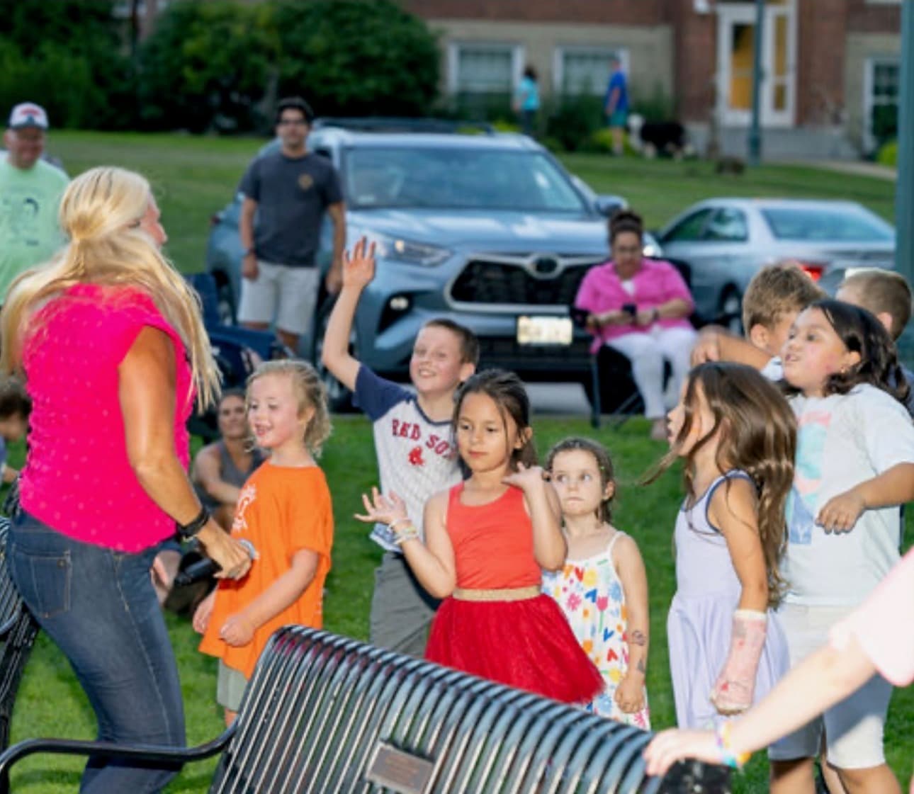 Singer reaching out to a group of kids at dusk, cars and houses in the background
