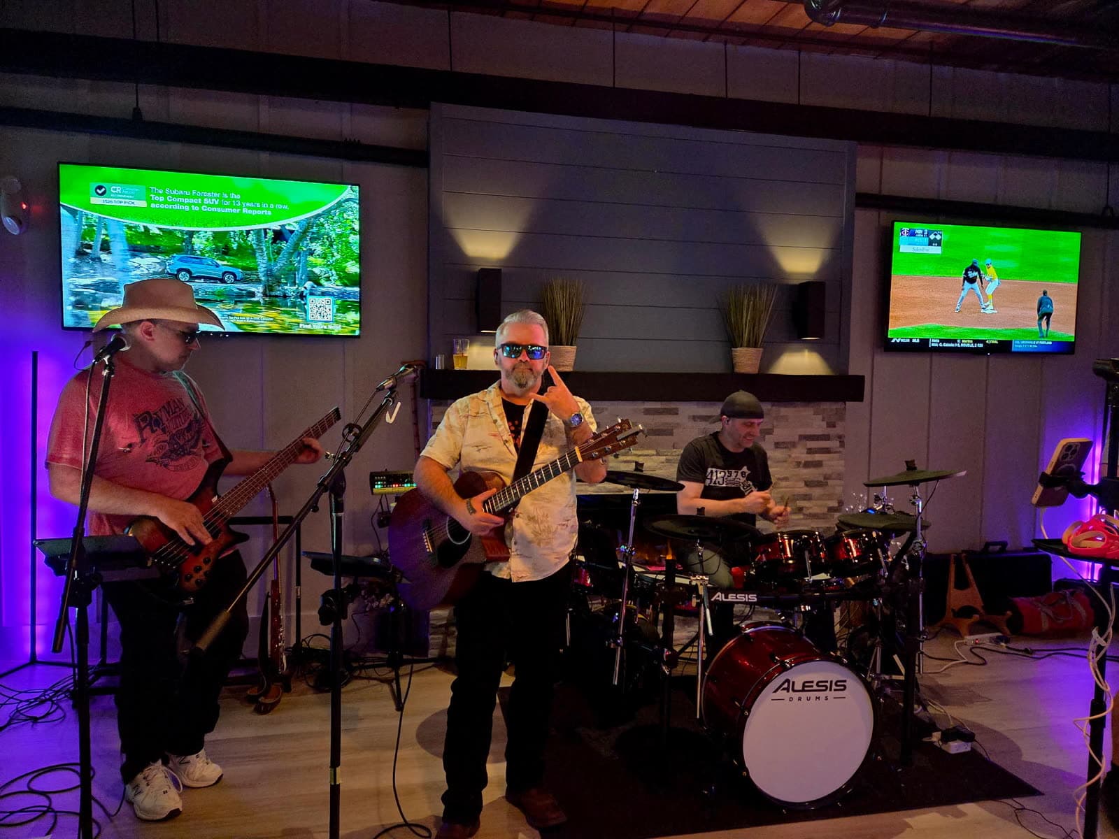 Bassist, guitarist, and drummer performing with a rock-on hand sign